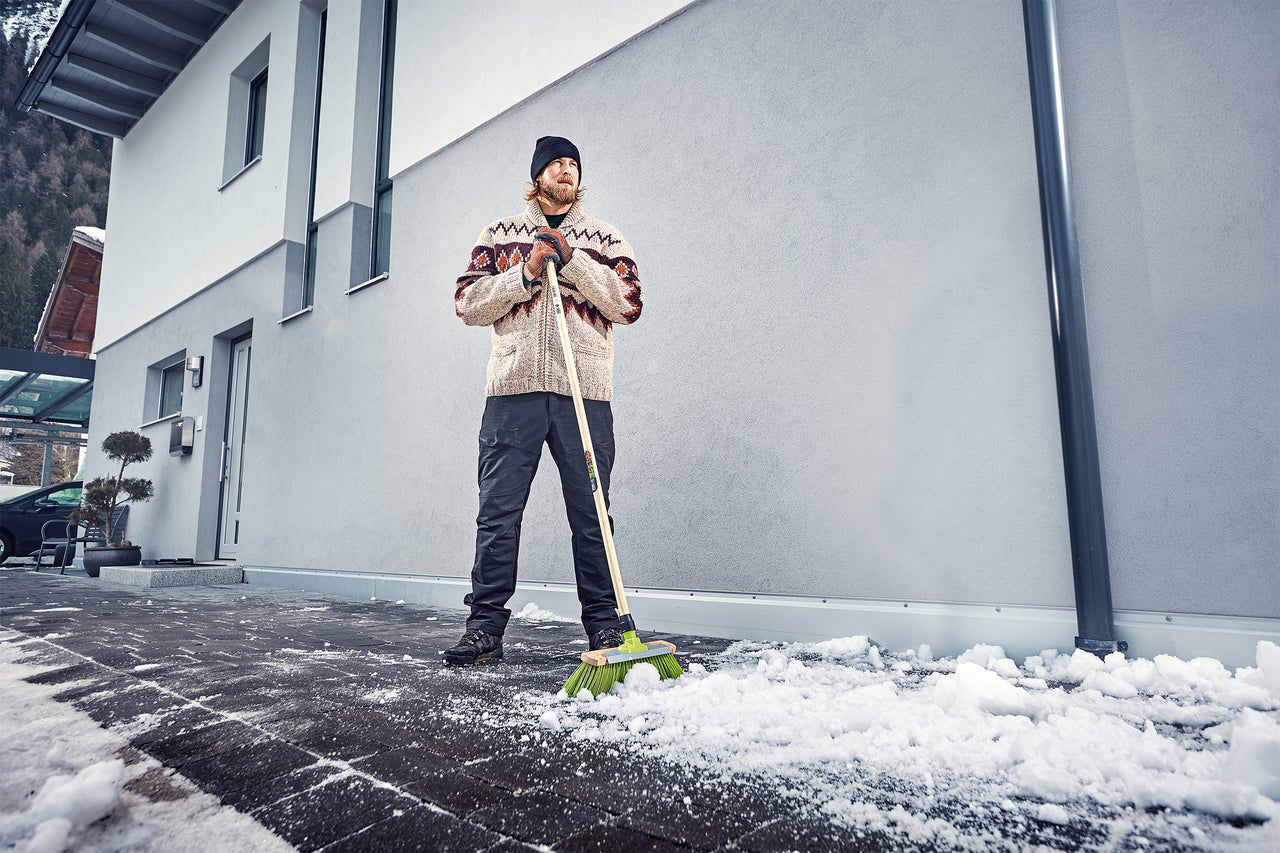 Man sopar snö med en gatusop framför ett hus.