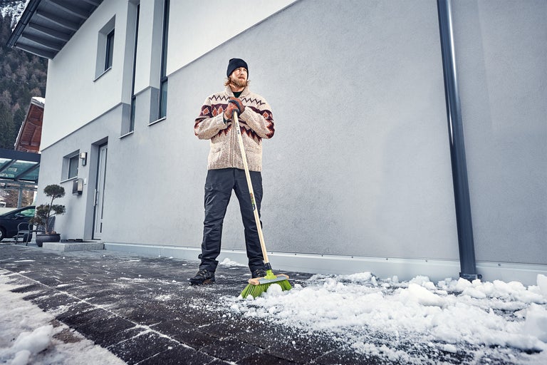 Man sopar snö med en gatusop framför ett hus.