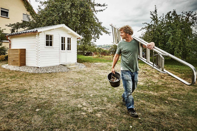 Man med stege och hink framför trädgårdshus