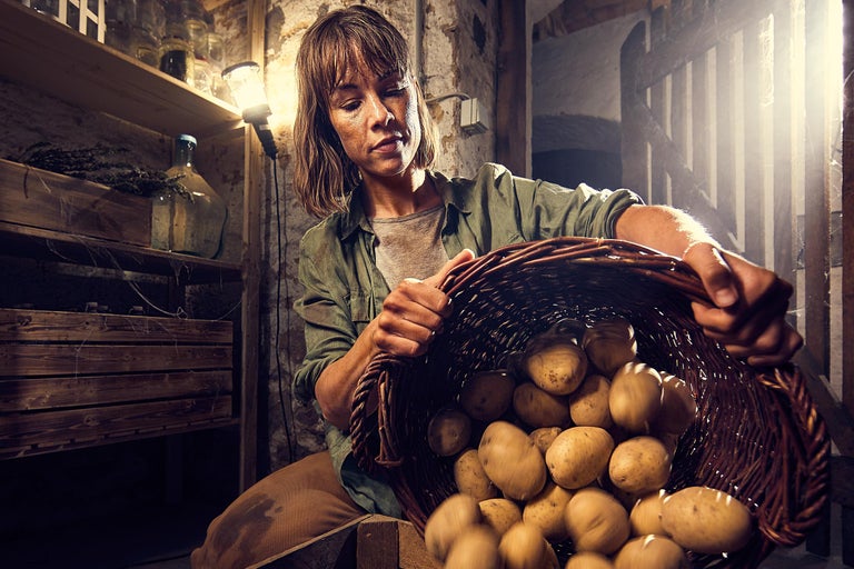 Kvinna håller en korg med potatis i källaren.