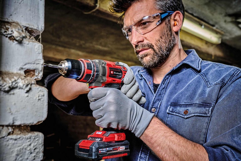 Man borrar i en tegelvägg med en sladdlös skruvdragare. Einhell logotyp.