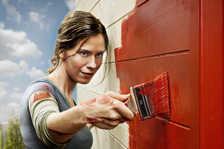 Kvinna målar träfasad med en pensel och träfärg