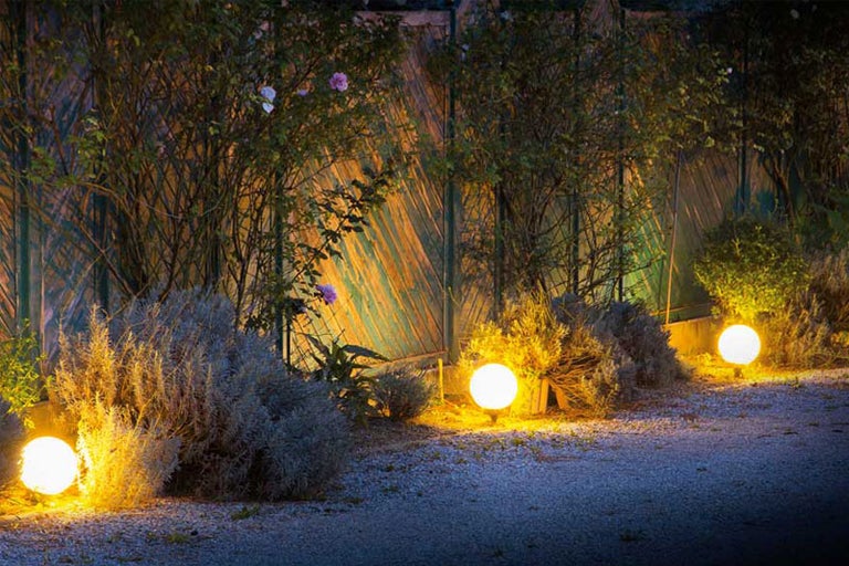 Trädgårdsvy med upplysta sfäriska lampor längs en stig.