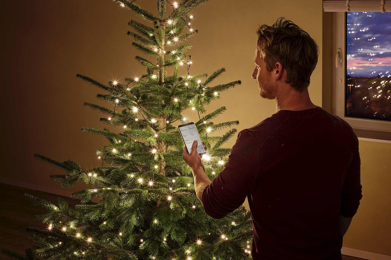 Man styr ljusslingan på julgranen med en smartphone.