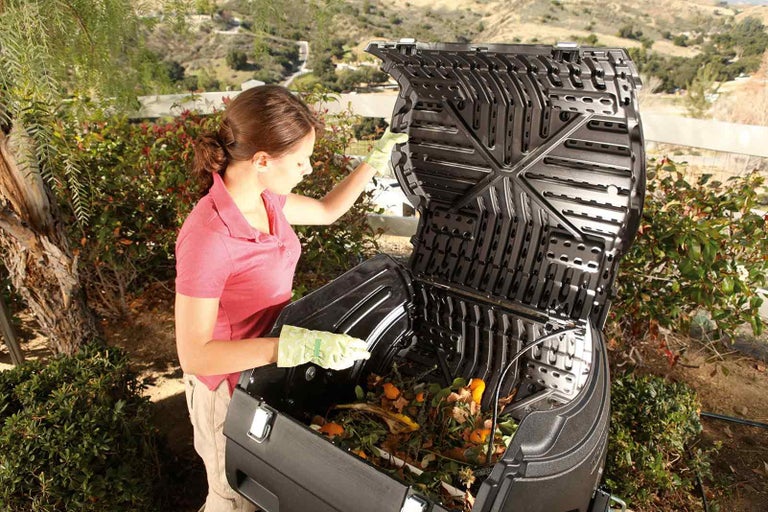 En kvinna fyller en kompost i trädgården med organiskt avfall.