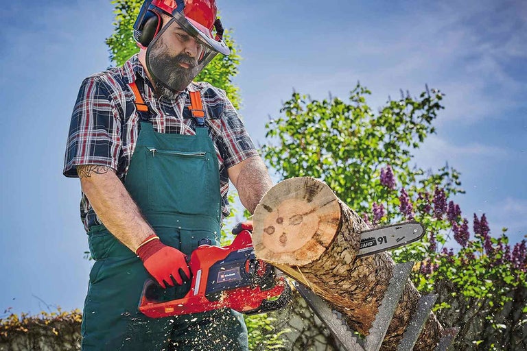 Man sågar trädstam med motorsåg, bär skyddskläder