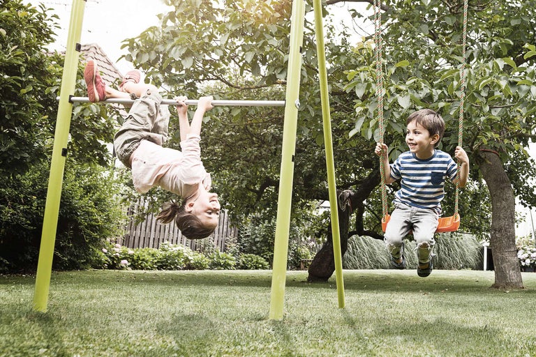 Barn leker på en gunga och en räckstång i trädgården.