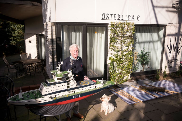 Man med fartygsmodell och hund framför hus med texten 'OSTERBLICK 6'