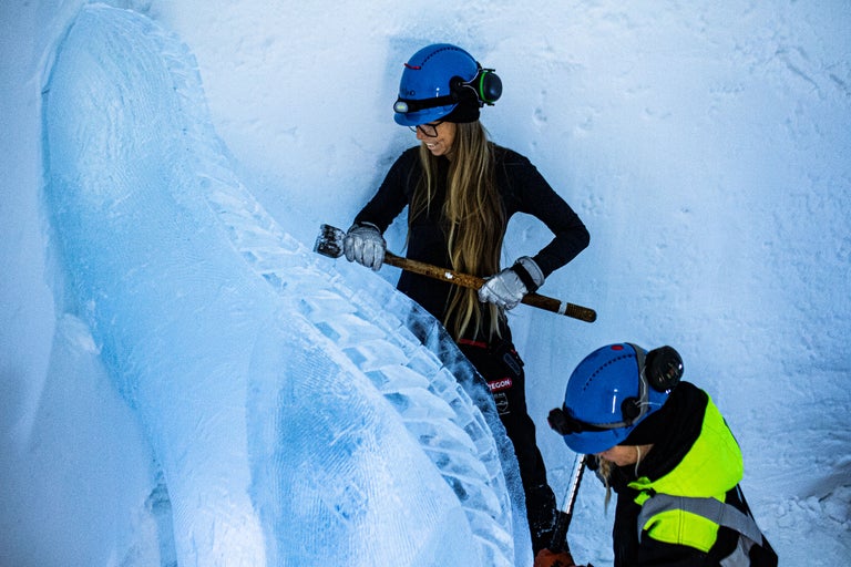 Isbergsklättrare med hjälm, handskar och ishacka som arbetar på en isvägg