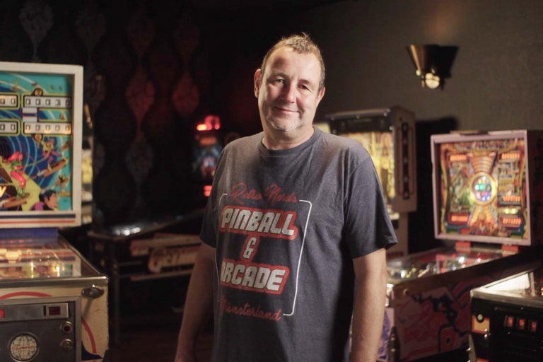En man står i ett rum med flera flipperspel.