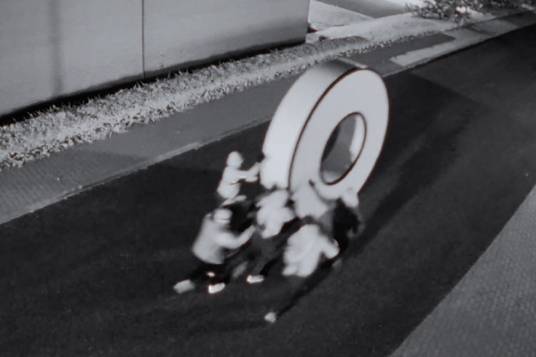 Personer flyttar ett stort ringelement på en väg.