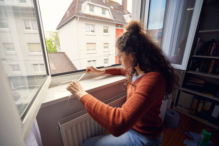 Kvinna fäster tätningsband på en fönsterkarm för fönstertätning