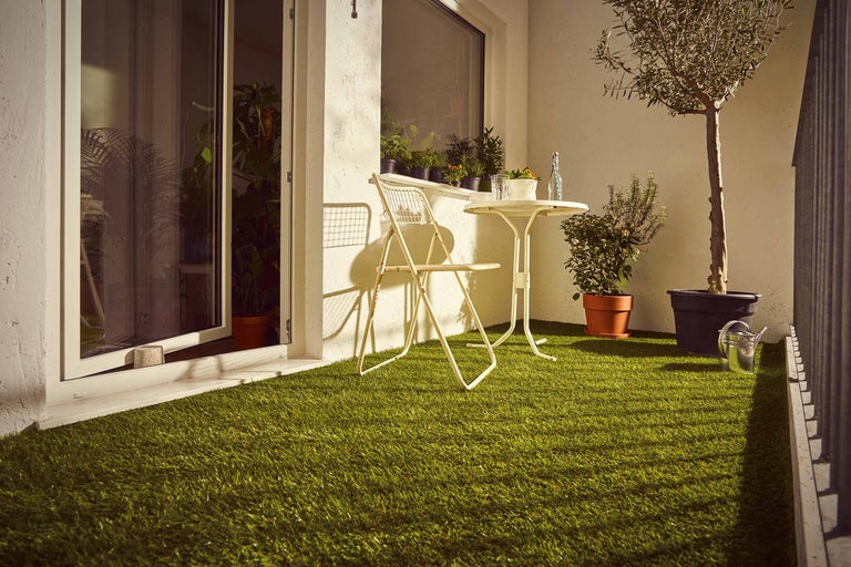 Balkong med konstgräs, stol, bord och växter