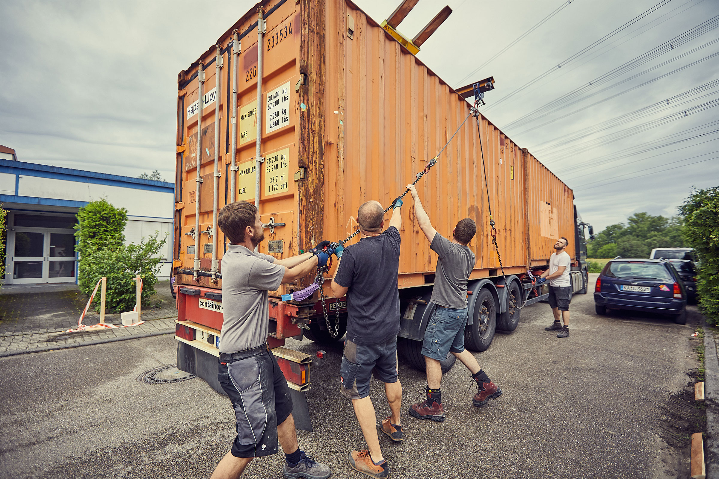 Män hänger en container med kedjor på en kran