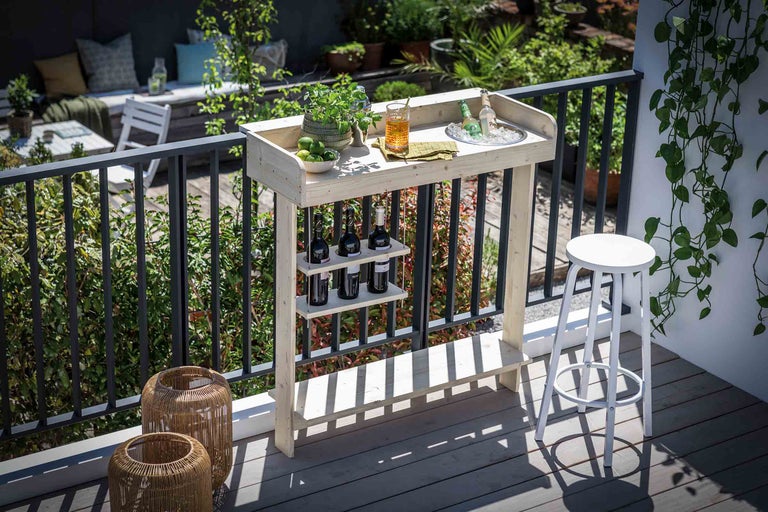 Barbord i trä med flaskhållare och pall på en balkong med växter