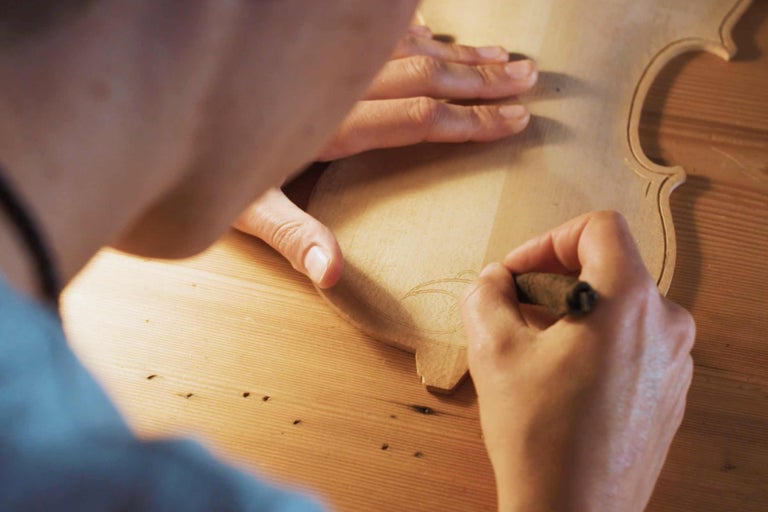 En person ritar ett mönster på en violin i trä.