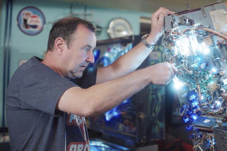 En man reparerar en flipperspel med kablar och lampor.