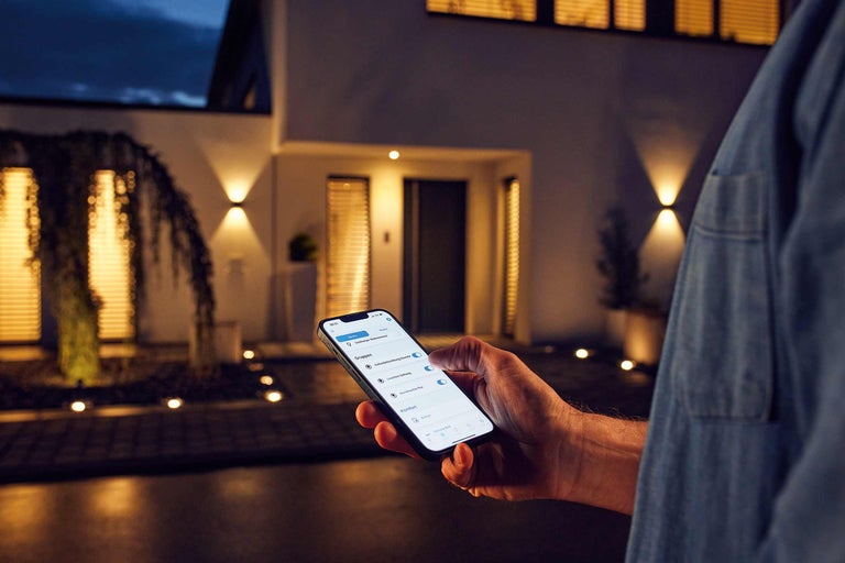 Person som styr utomhusbelysning via smartphone-app vid huset