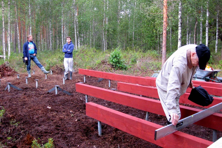 Tre personer bygger en grund av trä och metallstolpar i skogen.