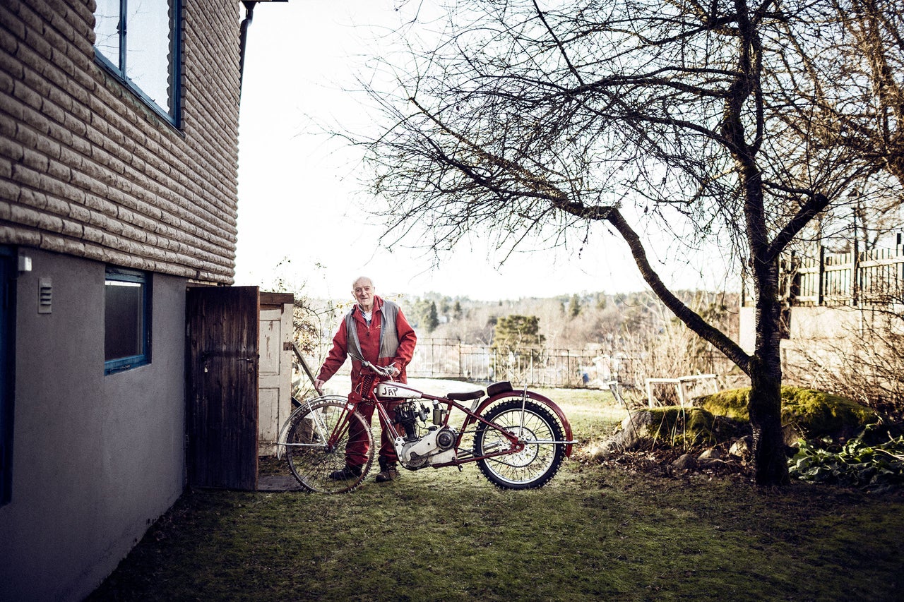 En man står bredvid en veteranmotorcykel framför ett hus på en gräsmatta