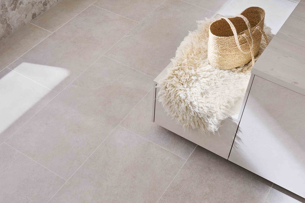 Beige golvplattor i ett rum med bänk, fårskinn och korg