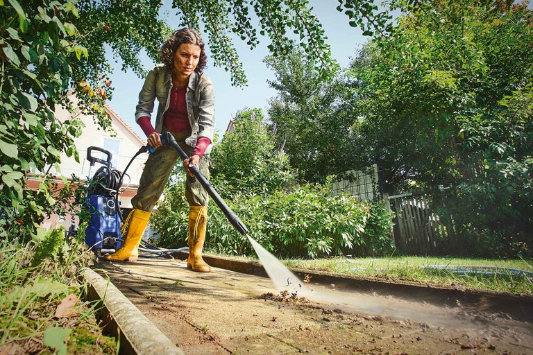 Kvinna rengör gångväg med högtryckstvätt i trädgården.