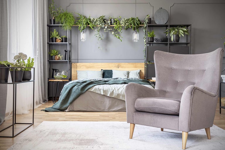 Sovrum med säng, fåtölj, hyllor och krukväxter