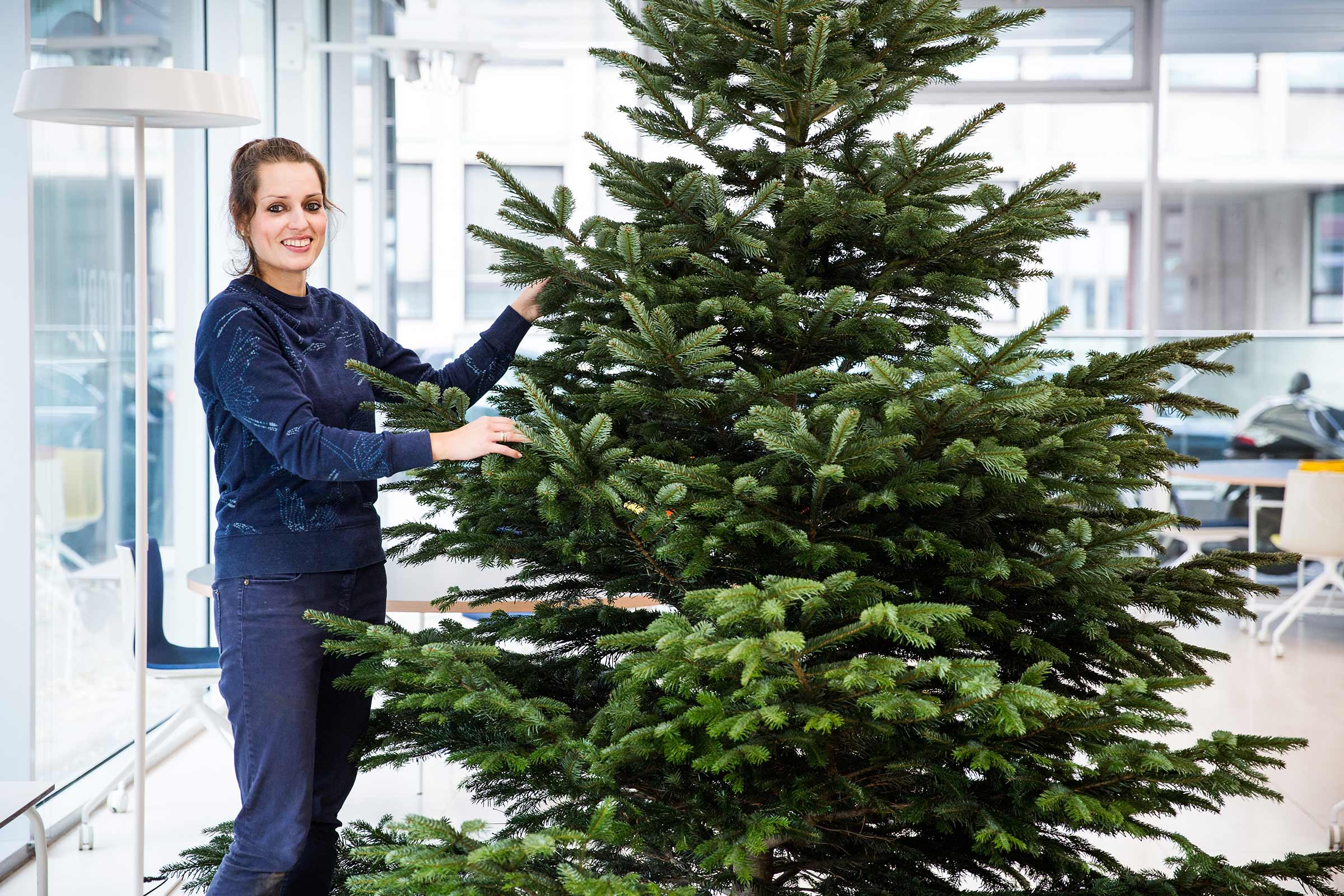 Kvinna står bredvid en grön julgran inomhus
