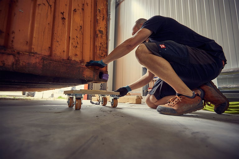 Man flyttar en container med en möbelrulle i en hall.