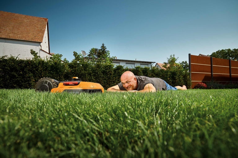 Man ligger avslappnad på gräsmattan bredvid en robotgräsklippare