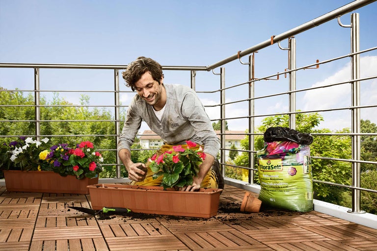 Man planterar blommor på en balkong med planteringsjord i en blomlåda.