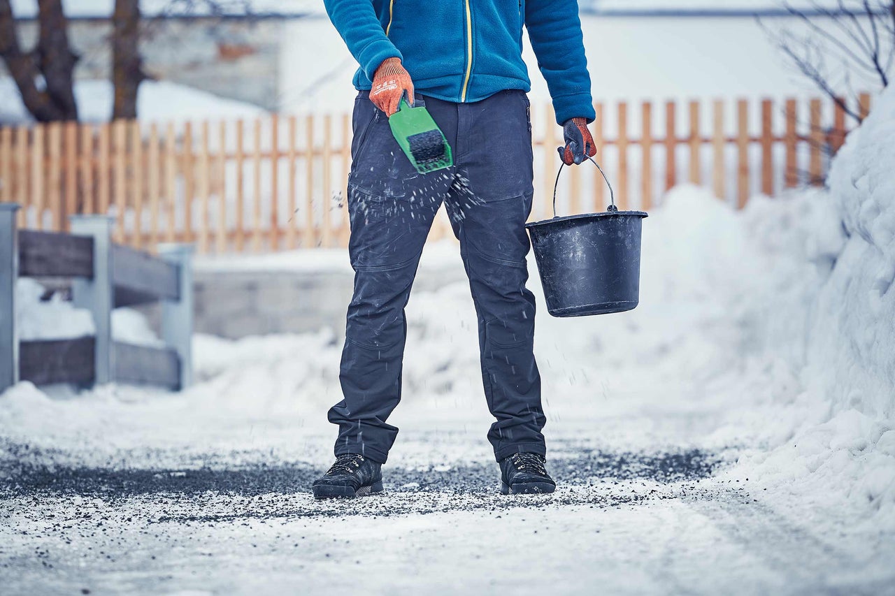 Man strör halkbekämpningsmedel med en skyffel på vintern