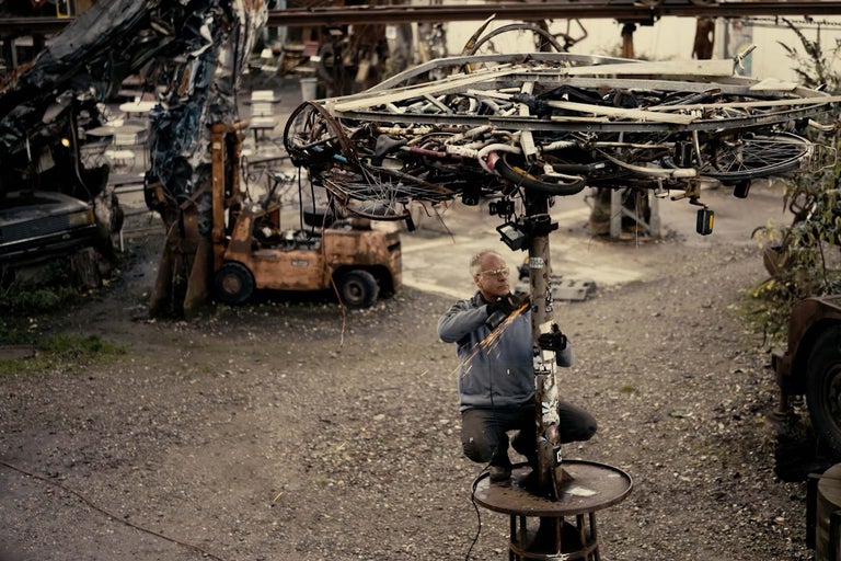 Man arbetar med en kapmaskin på en metallpelare under ett skydd av metallskrot.