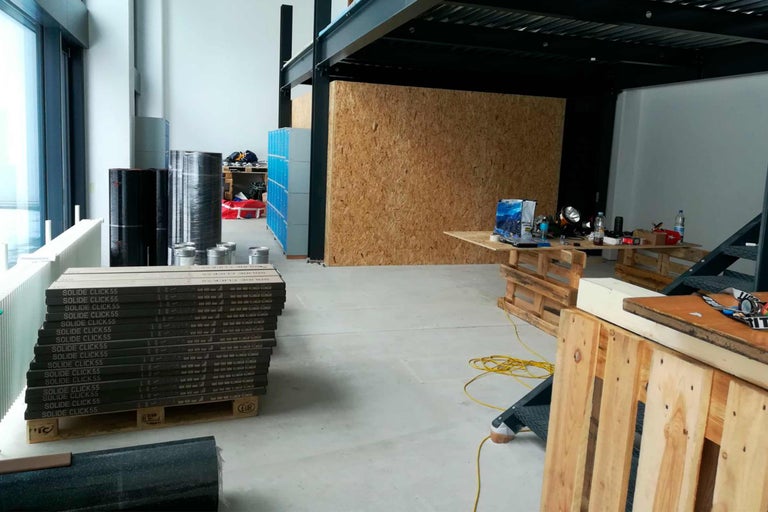 Interiörbild av ett rum med byggmaterial som golvplattor, isoleringsrullar och verktyg