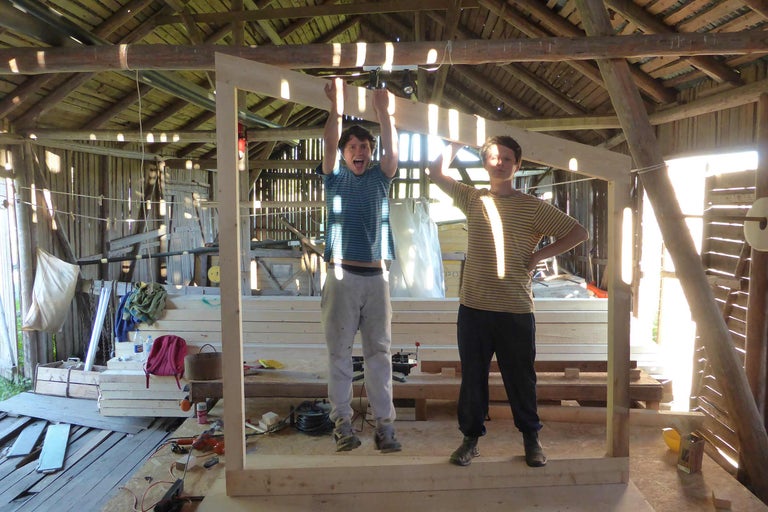 Två personer i en ljus träverkstad med träbjälkkonstruktion och träram