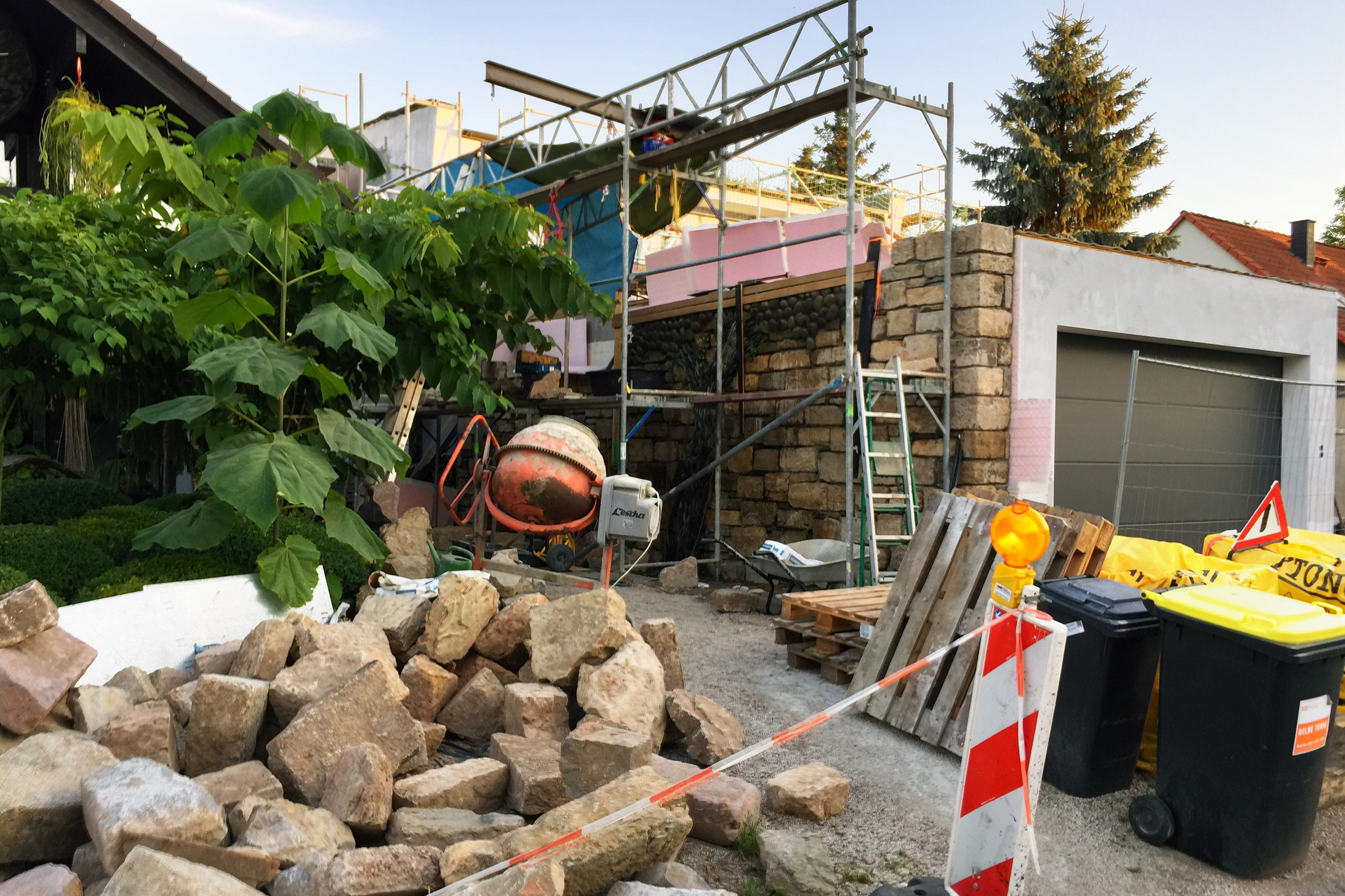 Byggarbetsplats med ställning, stenar, betongblandare och soptunnor