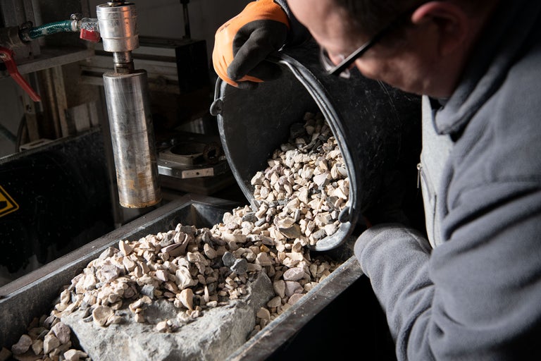 En person häller grus från en hink i en behållare.