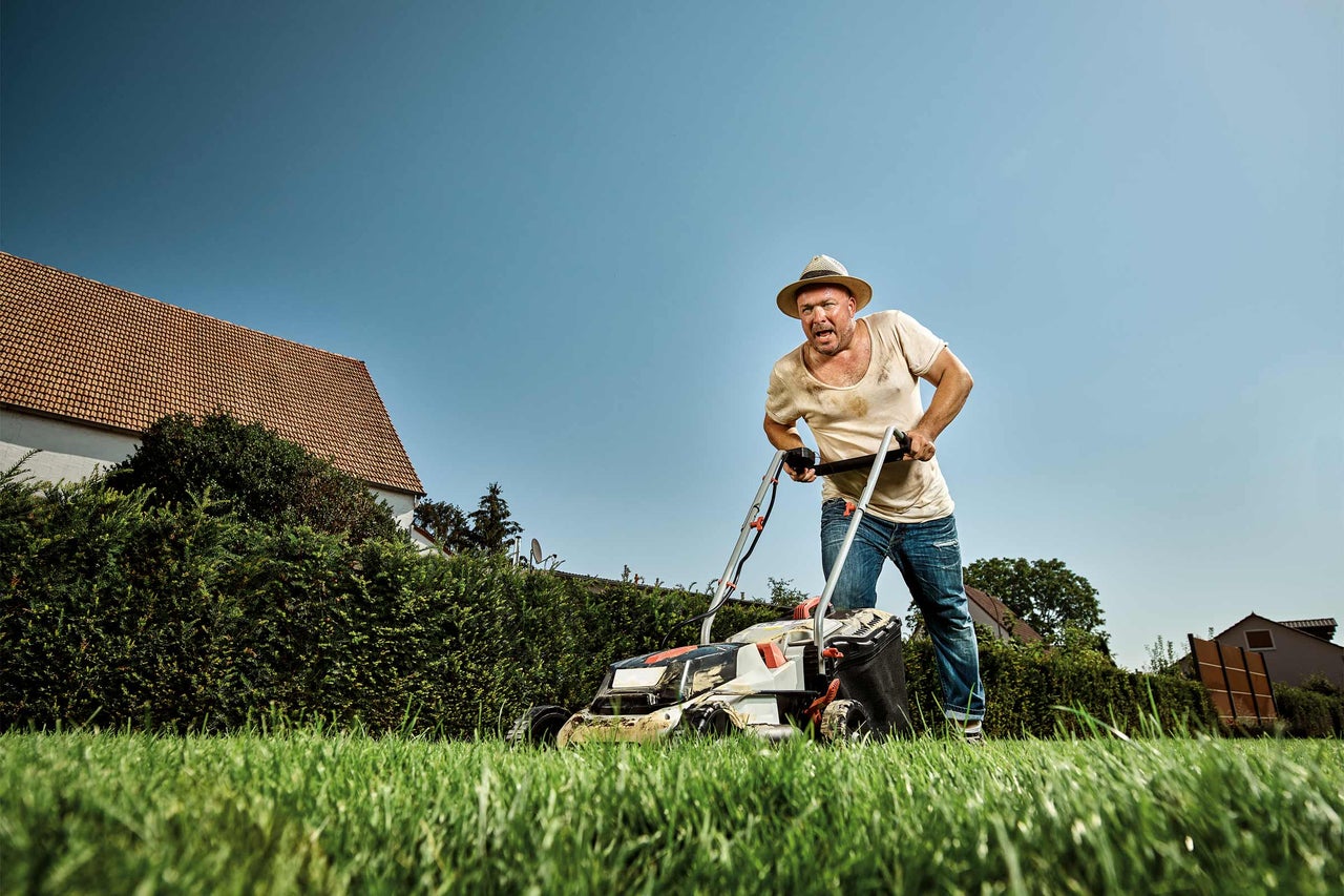 Man klipper gräs med en gräsklippare i trädgården.