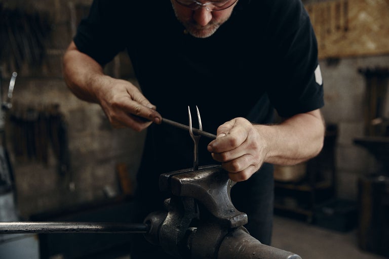 En man bearbetar metall med en fil i ett skruvstäd. Smide.