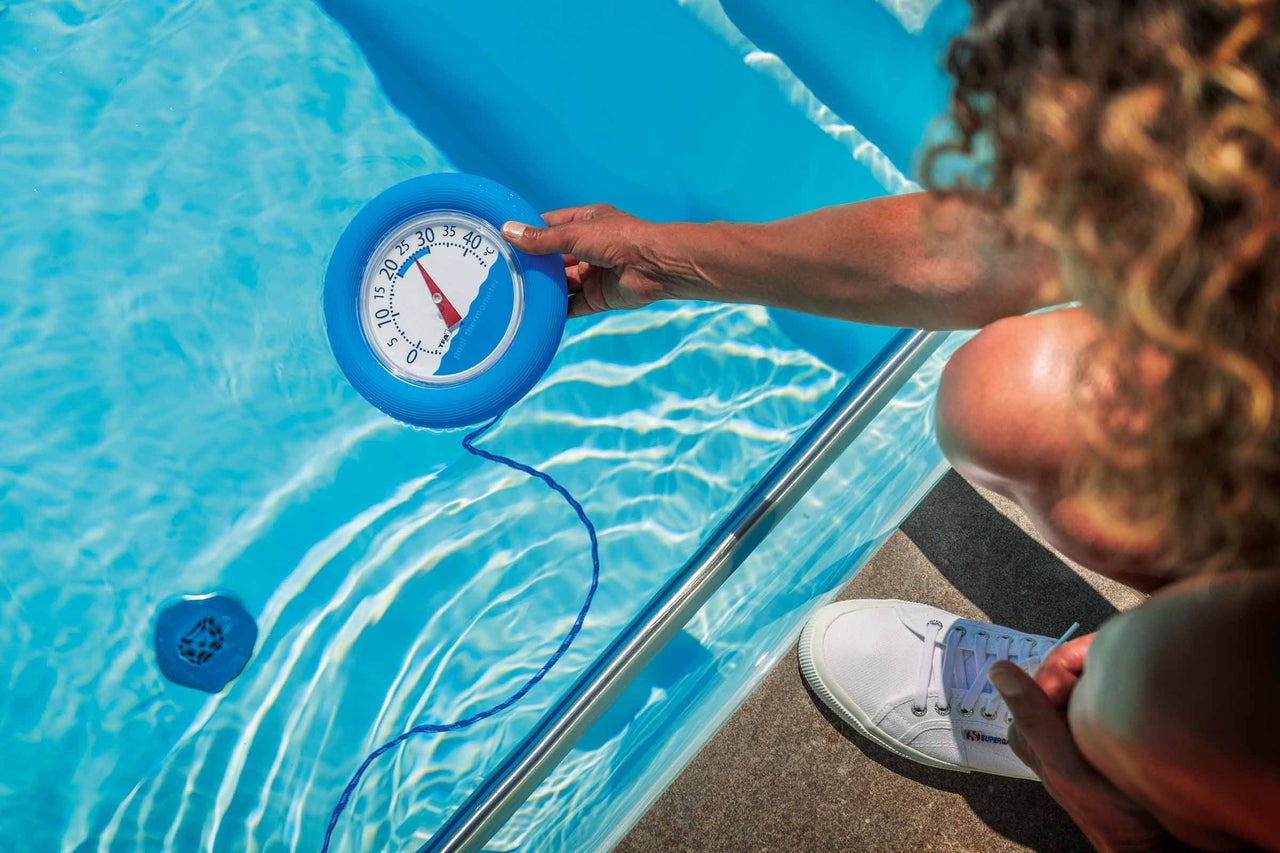 En person mäter temperaturen i en pool med en pooltermometer.