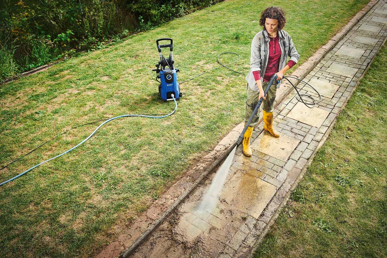 En kvinna rengör en trädgårdsgång med en högtryckstvätt.