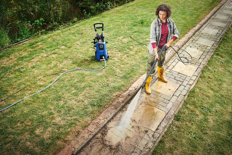 En kvinna rengör en trädgårdsgång med en högtryckstvätt.