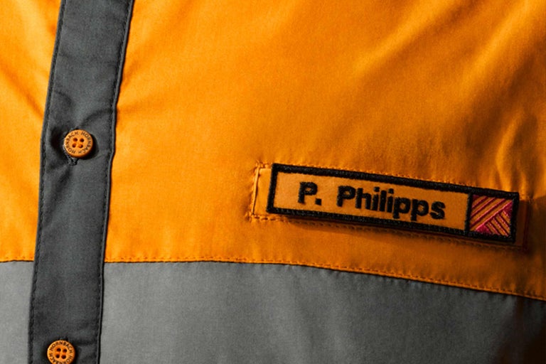 Närbild av en arbetsskjorta med namnskylt och Hornbach logotyp på knapparna