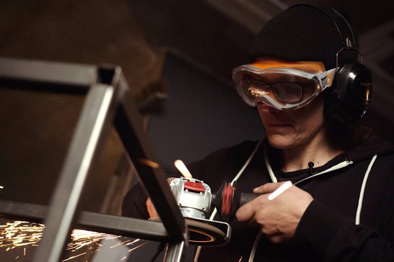 En person slipar metall med en vinkelslip medan gnistor sprutar. Personen bär skyddsglasögon och hörselskydd.