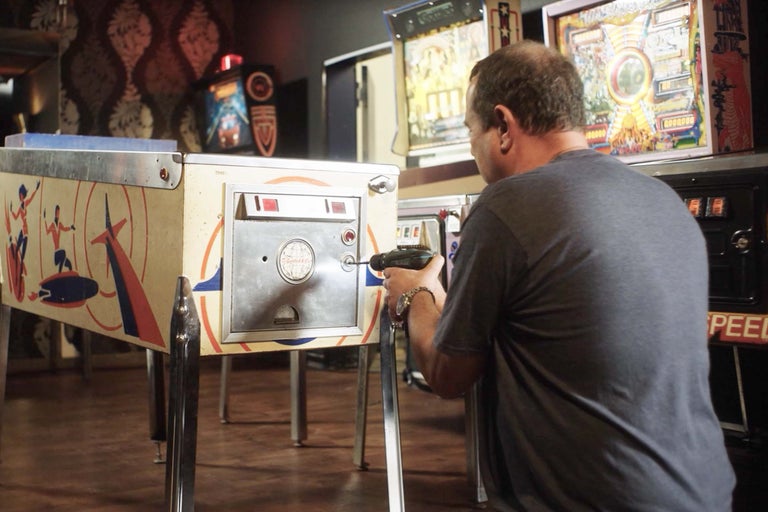 En man reparerar en flipperspel med en sladdlös skruvdragare i en spelhall