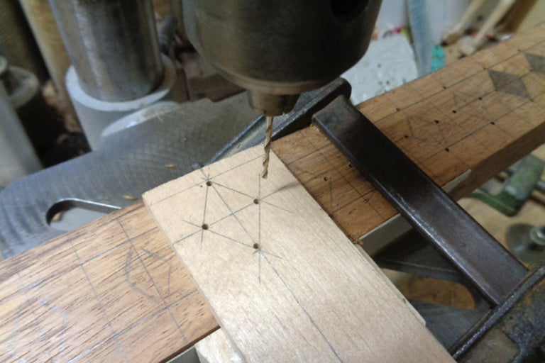 Närbild av en borrmaskin som borrar hål i en träplanka, fastsatt med en skruvtving.