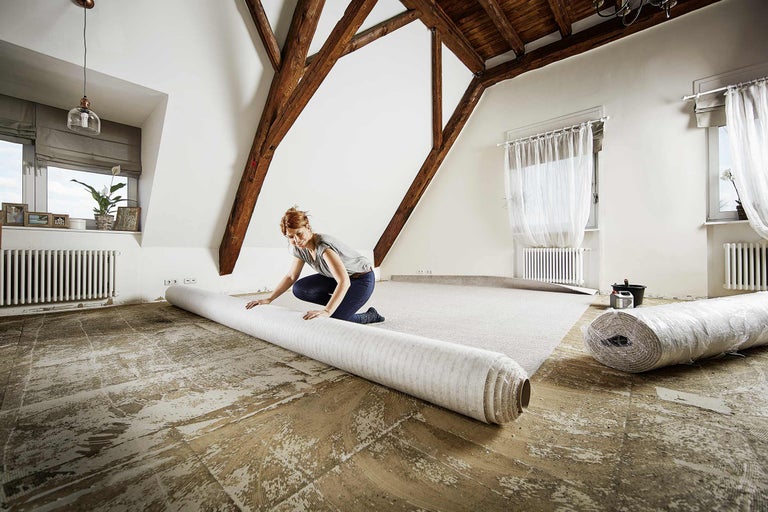 Kvinna lägger in en matta i ett ljust vindsrum med träbjälkar