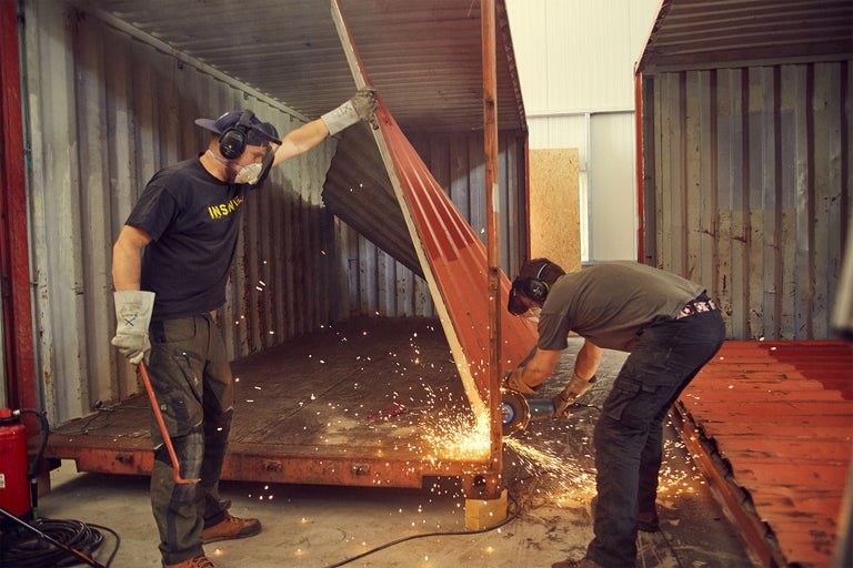 Två arbetare skär metall i en container med en vinkelslip, gnistor flyger.