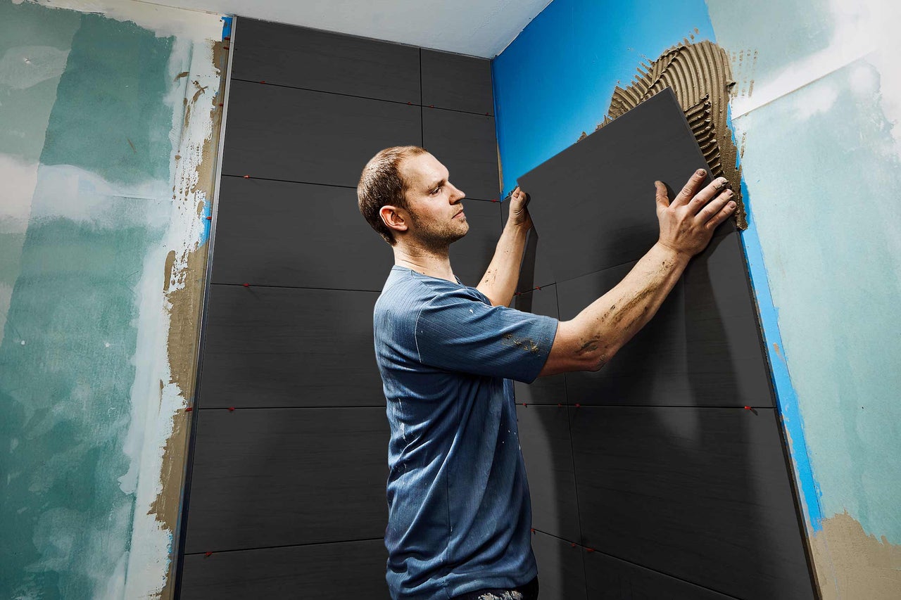 En man lägger kakel på en vägg i badrummet.