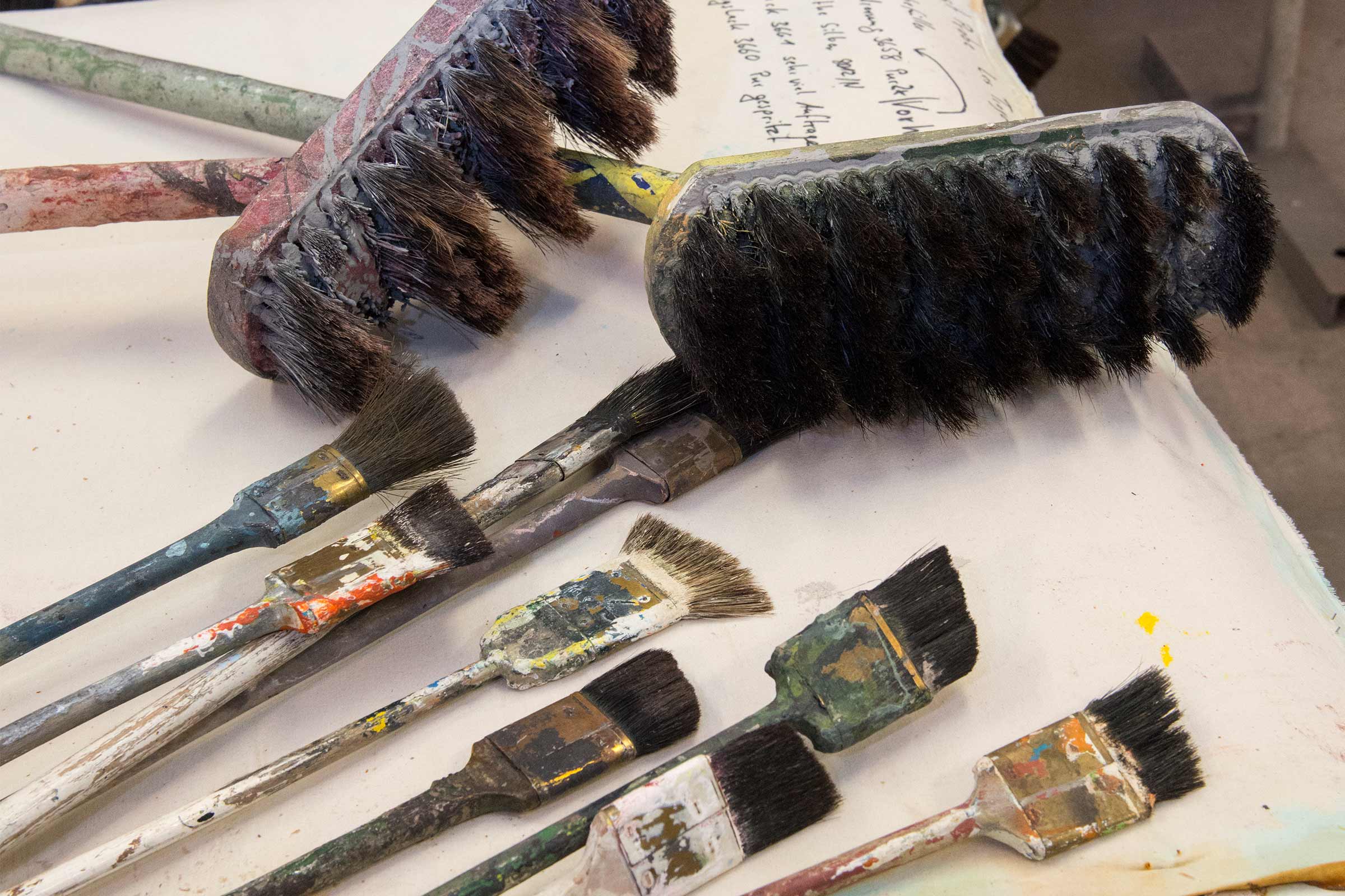 Flera använda penslar i olika storlekar och former ligger på en yta.